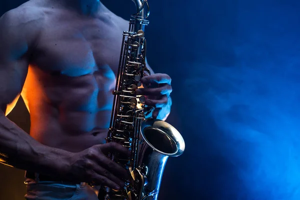 Muscular man with naked torso playing on saxophone with smoked colorful background — Stock Photo, Image