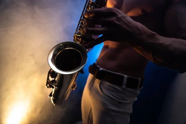 Homem muscular com tronco nu tocando no saxofone com fundo colorido fumado — Fotografia de Stock