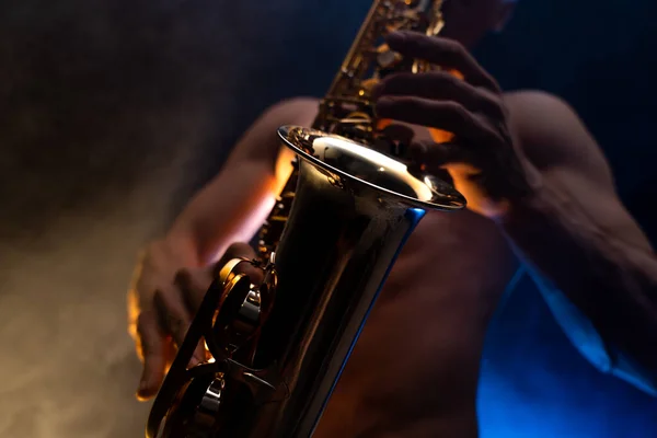 Muscular man with naked torso playing on saxophone with smoked colorful background — Stock Photo, Image