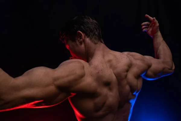 Muskulöser Mann, der auf dem schwarzen Hintergrund mit farbigem Rauch isolierte Muskeln zeigt. Konzept eines gesunden Lebensstils — Stockfoto