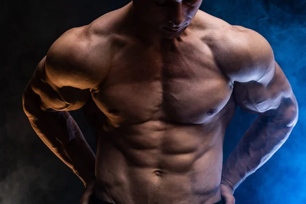 Hombre musculoso mostrando músculos aislados en el fondo negro con humo de color. Concepto de estilo de vida saludable — Foto de Stock