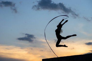 Gökyüzü arka planında kurdelesi olan profesyonel jimnastikçi kadın dansçı.