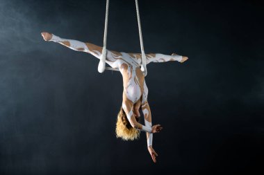 Genç bir kız akrobatik öğeleri hava trapez gerçekleştirir. Stüdyo performansları bir siyah arka plan üzerinde çekim