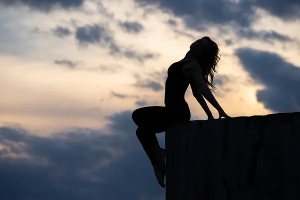 Mujer joven sentada en el borde con el fondo del amanecer. Concepto de libertad, estilo de vida valiente y feliz — Foto de Stock