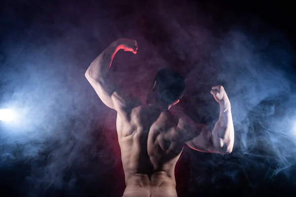 Hombre musculoso mostrando músculos aislados en el fondo negro. Concepto de estilo de vida saludable y salud — Foto de Stock