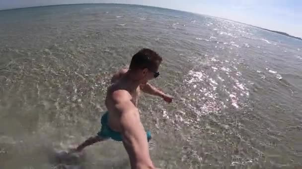 Hombre joven corriendo con palo selfie en la arena de playa de agua de mar de cristal poco profundo. Concepto de aventura y felicidad . — Vídeo de stock