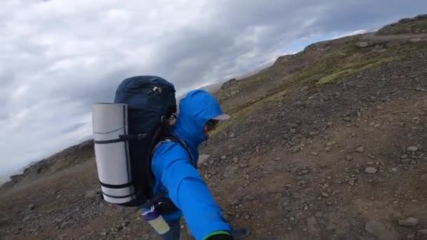 Sonriente Joven camina a través del terreno áspero de Islandia durante el fuerte viento hasta 30 mitras por segundo en la ruta de senderismo Fimmvorduhals — Vídeo de stock