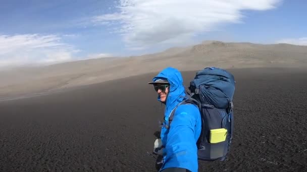 Leende Ung man vandrar genom tuff isländsk terräng under stark vind upp till 30 kvalster per sekund på Fimmvorduhals vandringsled — Stockvideo