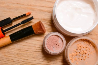 Dekoratif kümesi ve bakım kozmetik. Krema, pudra, allık, dudak parlatıcısı, fırça ve maskara ahşap arka plan, güzellik ve makyaj kavramı