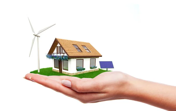 Maison avec éoliennes et panneaux solaires debout sur la main Image En Vente