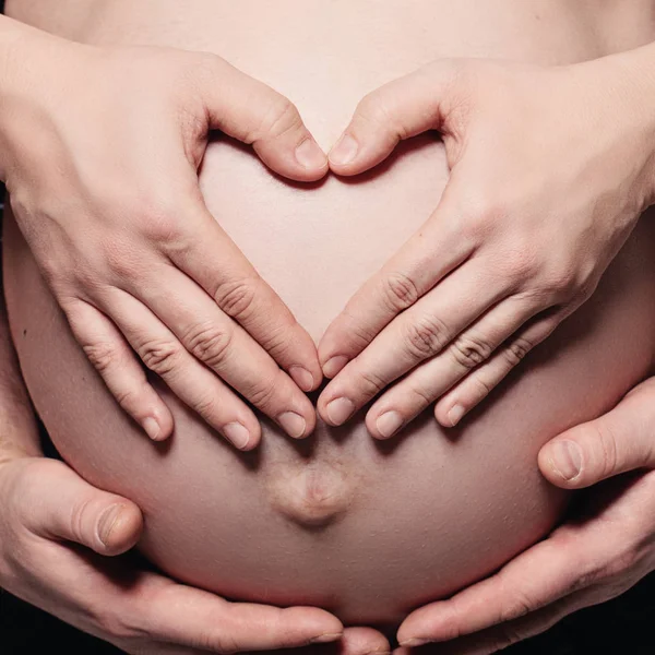 Mulheres grávidas barriga com as mãos masculinas e femininas fazendo um coração — Fotografia de Stock