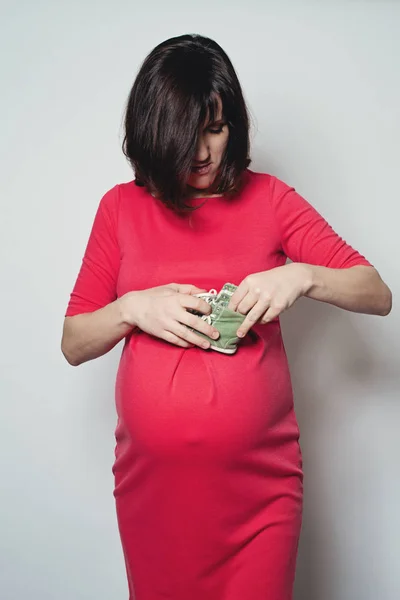 Kırmızı elbiseli küçük bebeğin ayakkabıları tutan hamile kadın — Stok fotoğraf