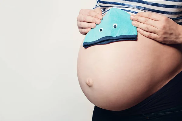 Una mujer embarazada. Estómago femenino y sombrerito azul sobre fondo —  Fotos de Stock