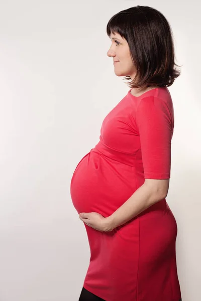 Schwangere in rotem Tuch auf grauem Hintergrund — Stockfoto