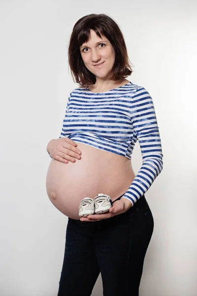 Gri arka plan üzerinde küçük ayakkabı ile hamile kadın — Stok fotoğraf