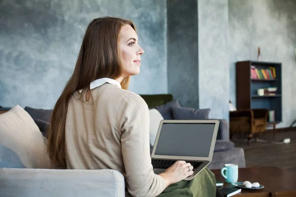 Ung kvinna använder laptop medan du sitter på bekväm soffa — Stockfoto