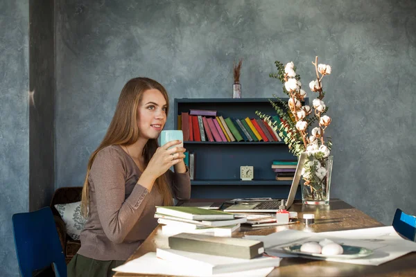 Cute Woman Sitting in Office, Drinking Coffee and Using Laptop