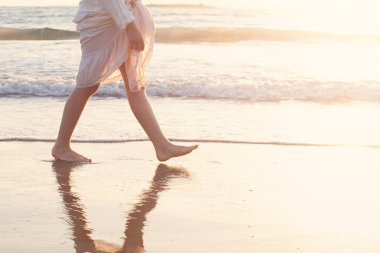 Güzel bir kadın gün batımında deniz sörfüyle sahilde yürür.