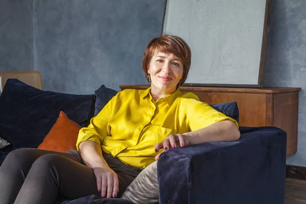 Happy middle aged woman sitting on sofa at home — Stock Photo, Image