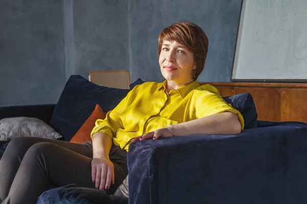 Mature woman sitting on velvet sofa at home — ストック写真