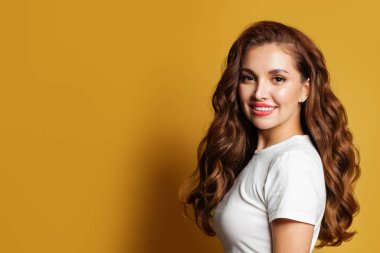 Uzun kahverengi kıvırcık saçlı, güzel, gülümseyen bir kadın.