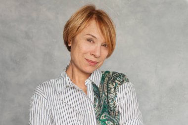 Gri saçlı, kısa kızıl saçlı, orta yaşlı güzel bir kadın. 