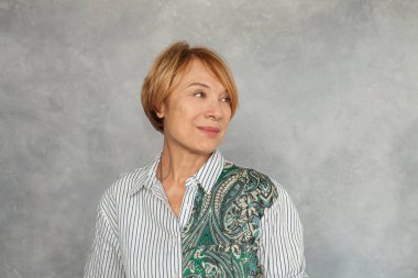 Güzel orta yaşlı kadın gri arka plana bakıyor.