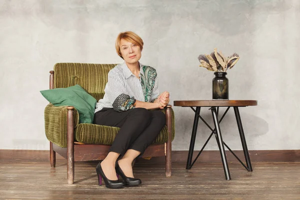 Perfect middle aged woman sitting on green armchair — Stock Photo, Image