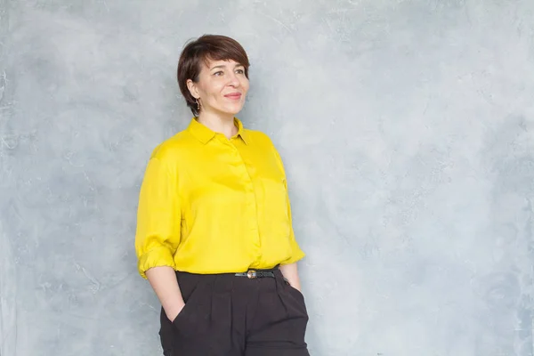 Pretty middle aged business woman in yellow shirt on gray — ストック写真