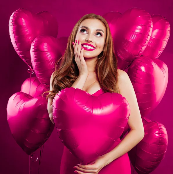 Pretty young woman with makeup and long ginger hair holding pink heart balloon on pink card backgroud — Stock Photo, Image