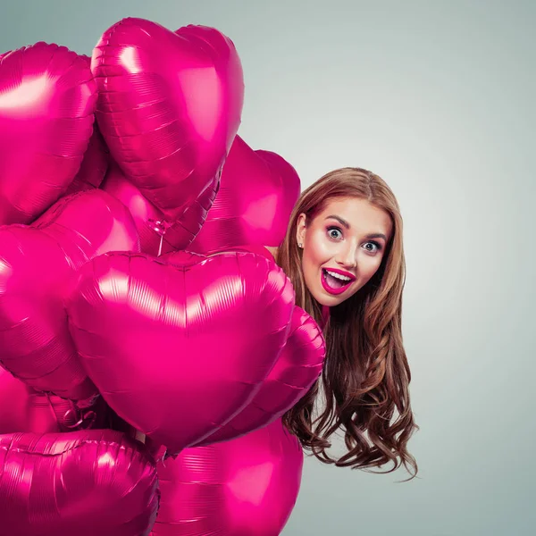 Hezká žena vykoukne z růžového srdce balónky a směje se — Stock fotografie