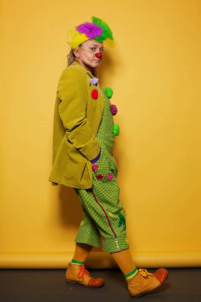 Performance Actriz mujer vistiendo traje de payaso colorido sobre fondo amarillo brillante — Foto de Stock