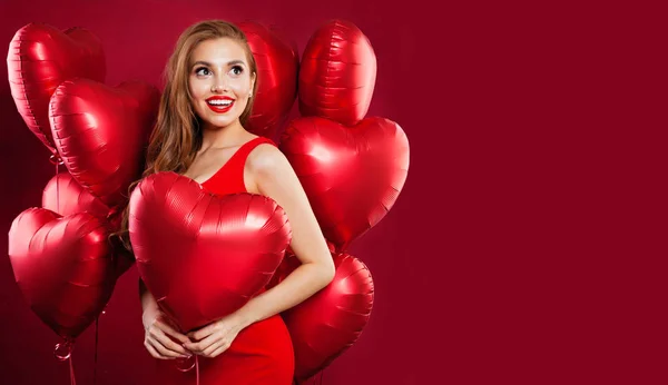 Trevlig ung kvinna med röda ballonger poserar på röd bakgrund — Stockfoto