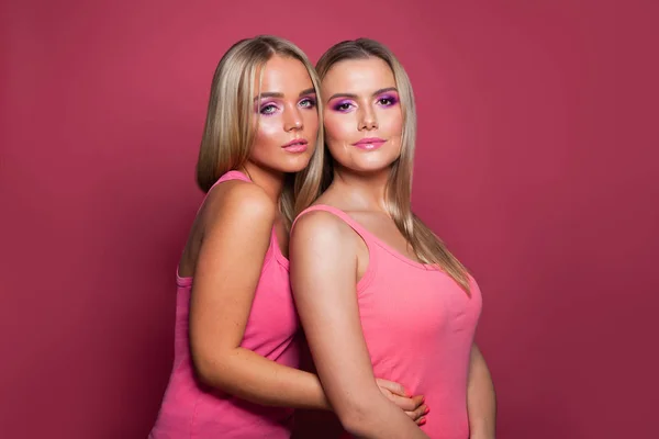 Twee mooie blonde meisjes dragen roze shirt op roze achtergrond — Stockfoto