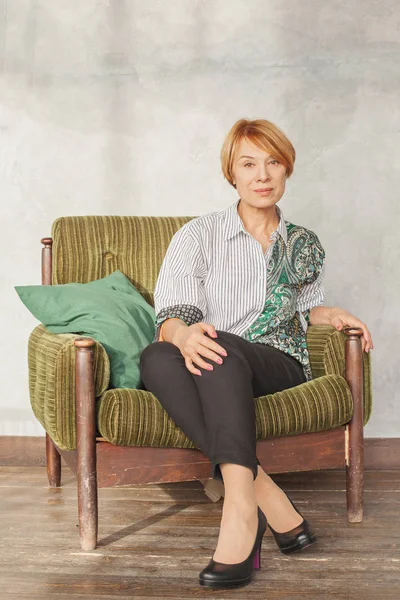 Dojrzałe kobieta z krótkim rude włosy siedzi na zielony fotel — Zdjęcie stockowe