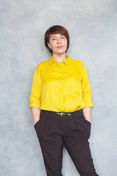 Confident business woman wearing yellow shirt standing on gray — Stok fotoğraf