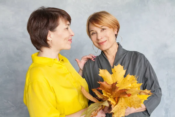 Autumn portrait of two mature women with fall maple leaves — Stok fotoğraf
