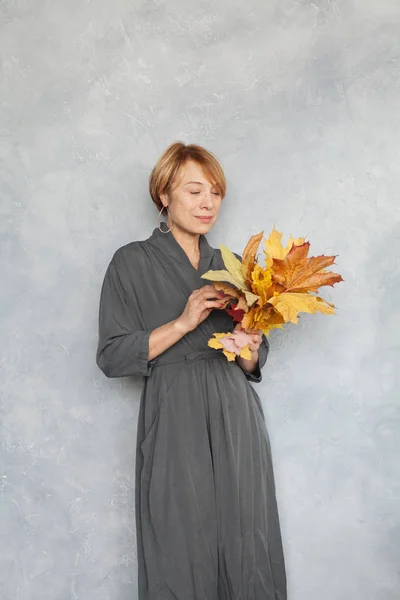 Ältere Frau mit kurzen Ingwerhaaren hält Herbst-Ahornblätter, s — Stockfoto