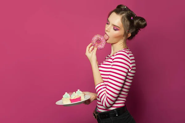 可愛いですモデル女性楽しんでドーナツ上のカラフルなピンクの背景 — ストック写真