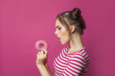 Genç bir kadın parlak pembe arka planda donut tutuyor.