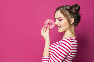 Güzel bir kadın donut tutuyor ve pembe arka planda eğleniyor.