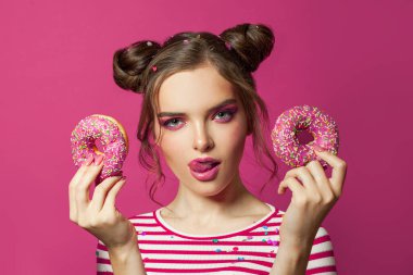 Renkli pembe arka planda donut tutan güzel bir model kadın.