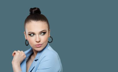 Zarif esmer kadın gülümsüyor ve mavi arka plana bakıyor.