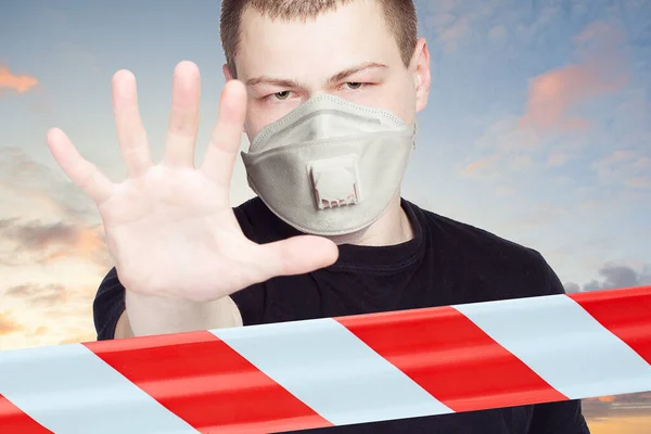 Man in a face mask showing stop gesture with warning tape outdoors
