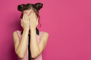 Güzel bir kadın parlak pembe arka planda yüzünü gizliyor.