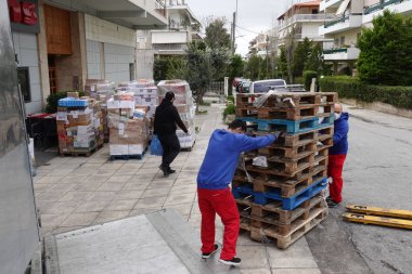 Atina, Yunanistan - 16 Mart 2020: Coronavirus covid-19 salgını sırasında alışveriş torbası ve cerrahi maske takan depo çalışanlarına sahip süpermarket müşterisi kamyondan gıda ürünlerinin kutularını boşalttı.