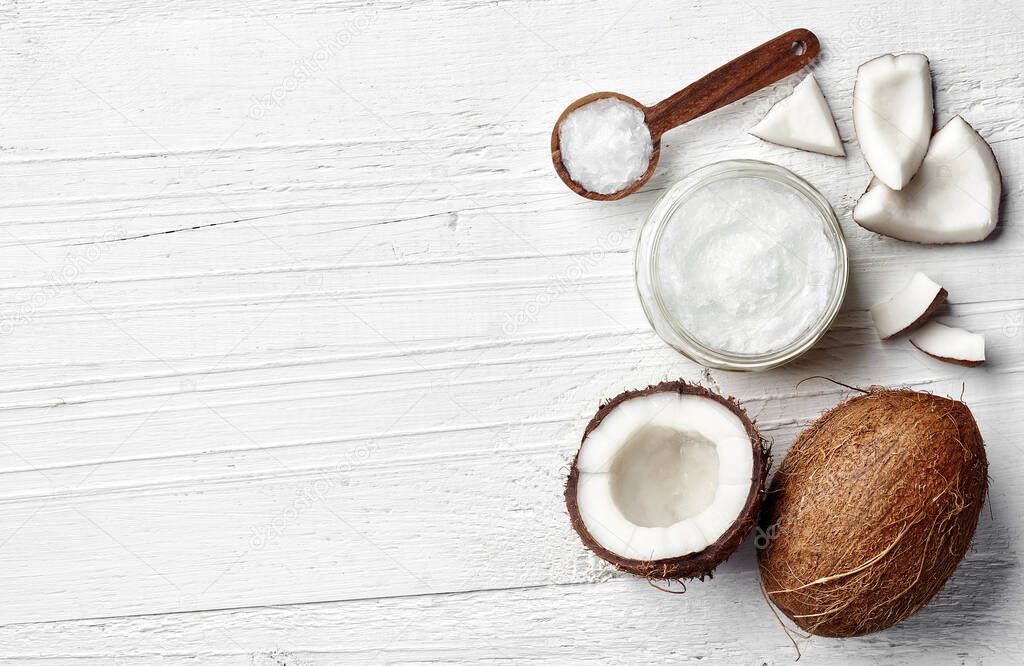 Jar of coconut oil and fresh coconut on white wooden background, top view