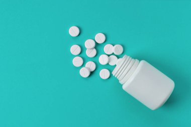 Mavi arka planda, beyaz yuvarlak haplar şişeden dökülüyor. Üst manzara, mesaj için boş alan.