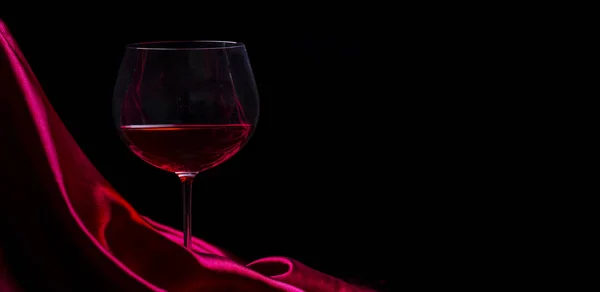 Glass of red wine on red silk against black background. Wine lis — Stock Photo, Image