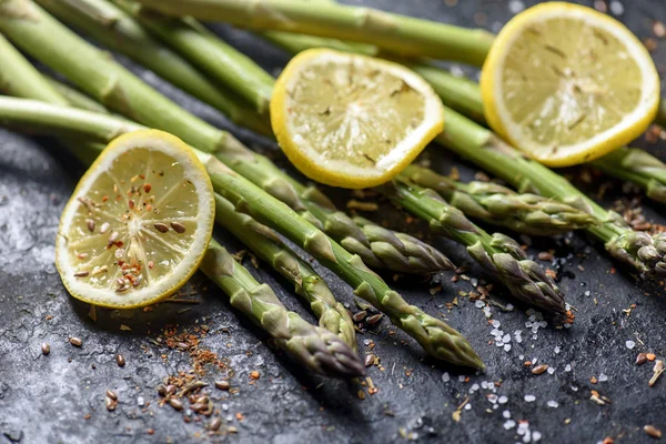 Färsk sparrisrätt med citron och kryddor på svart tallrik closeu — Stockfoto